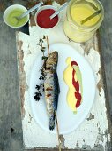 Sardines on wooden board with three sauces, overhead view