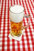 Bier in großem Glas mit Henkel steht auf Tischdecke.
