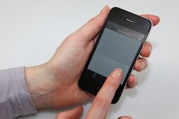Frauenhand hält Apple iPhone und berührt Display.