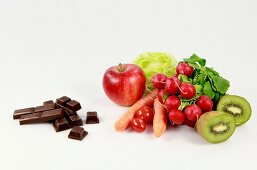 Various fruits next to pieces of chocolates on white background