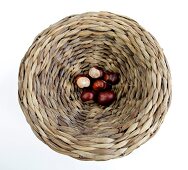 Chestnuts in wicker basket on white background, overhead view