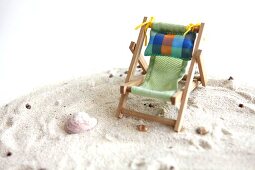 Close-up of small deck chair on sand with sea shells