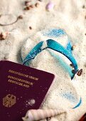 Close-up of flip flop and passport in the sand with sea shells
