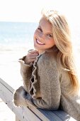 Portrait of beautiful blonde woman wearing brown knitted jacket standing on beach