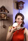 Beautiful woman wearing orange top holding doughnut with cream standing near cuckoo clock