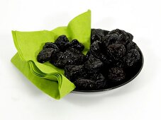 Dry plums with green cloth in bowl on white background