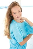 Portrait of beautiful blonde woman wearing turquoise top with hand in hair, smiling