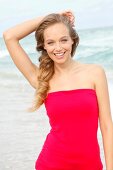 Portrait of beautiful blonde woman wearing red dress standing on beach, smiling