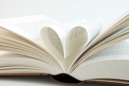 Close-up of open book with pages folded in heart shape on white background