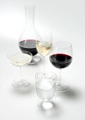 Carafe, shot glass and wine glasses with red and white wine on white background