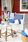 Flowers on a side table and homemade blue and white cushions on a wooden bench on a summery terrace