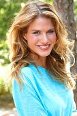 Portrait of beautiful blonde woman with long wavy hair wearing blue top, smiling