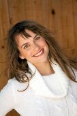 Happy woman in white turtleneck sweater standing in front of wooden wall and smiling