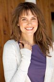 Portrait of pretty brown haired woman wearing purple top and white cardigan, smiling