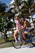 Paar hat Spaß auf einem Rad sie sitzt auf Lenker, Palmen