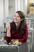 Portrait of pretty woman with brown hair in red blouse eating at restaurant, smiling