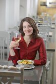 Pretty woman holding a glass of white wine with both hands in restaurant, smiling