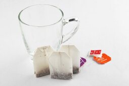 Glass tea cup with three tea bags on white background
