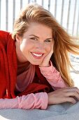 Portrait of attractive woman wearing red sweater and pink top lying on sand, smiling