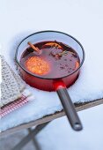 A saucepan of mulled wine and orange slices in the snow