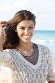 Dark-haired woman in a V-neck mesh sweater, laughing by the sea