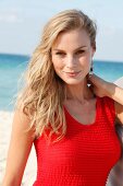 Blonde woman in a red dress on the beach, smiling and looking at camera