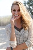 Portrait of pretty blonde woman wearing jumper with v neck standing on beach, smiling