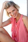 Portrait of beautiful blonde woman in pink top, stroking hair back, smiling