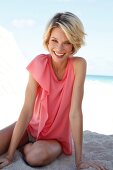 Portrait of happy woman wearing pink top sitting on sand, smiling