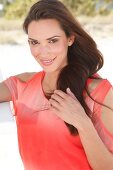 Portrait of beautiful woman with dark hair in red top standing with hands on hip, smiling
