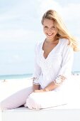Portrait of happy woman wearing white tunic blouse sitting on beach, smiling