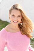 Portrait of beautiful blonde woman wearing pink sweater standing near wall, smiling