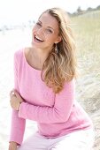 Portrait of cheerful woman wearing pink sweater sitting in sand, smiling