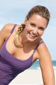blonde Frau im lila Sportoutfit am Strand, lacht in die Kamera