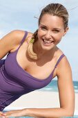 blonde Frau im lila Sportoutfit am Strand, lacht in die Kamera