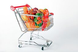 Shopping cart with vegetables and fruits on white background