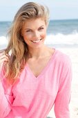 Portrait of pretty blonde woman wearing pink sweater sitting on beach, smiling