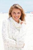 Portrait of blonde woman wearing white turtleneck sweater standing on beach, smiling