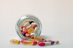 Different pills, tablets, dragees and capsules spilling out from glass bottle