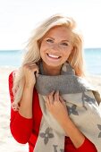 blonde Frau im roten Pulli lächelt in Kamera, am Strand