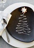 A plate decorated for Christmas with a writing icing Christmas tree and a cinnamon star biscuit on top