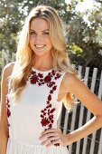 Blonde Frau mit langen Haaren in Sommerkleid am Strand vor Zaun