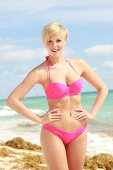 Blonde Frau mit kurzen Haaren im pinkfarbenem Bikini am Strand