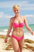 Blonde Frau mit kurzen Haaren im pinkfarbenem Bikini am Strand