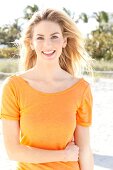 Blonde Frau mit langen Haaren in orangefarbenem T-Shirt am Strand