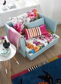 Sessel mit bunten, floral gemusterten Kissen, Retro Beistelltisch und gemusterter Teppich in einem Wohnzimmer