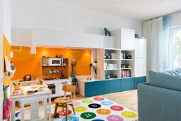 Spielecke im Wohnzimmer - mit Miniküche zwischen Schrankelementen und Kindertisch auf Teppich mit buntem Knopfmuster