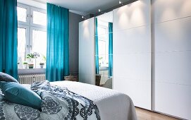Weisser Kleiderschrank mit breiten Schiebelementen und Spiegelfront im Schlafzimmer mit blauen Vorhängen
