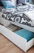 Ornamental patterned bedclothes on a double bed with an open drawer
