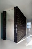 Minimalistischer Flur mit weißem Boden und geschlossenem Treppenhaus mit schwarzen Wandfliesen